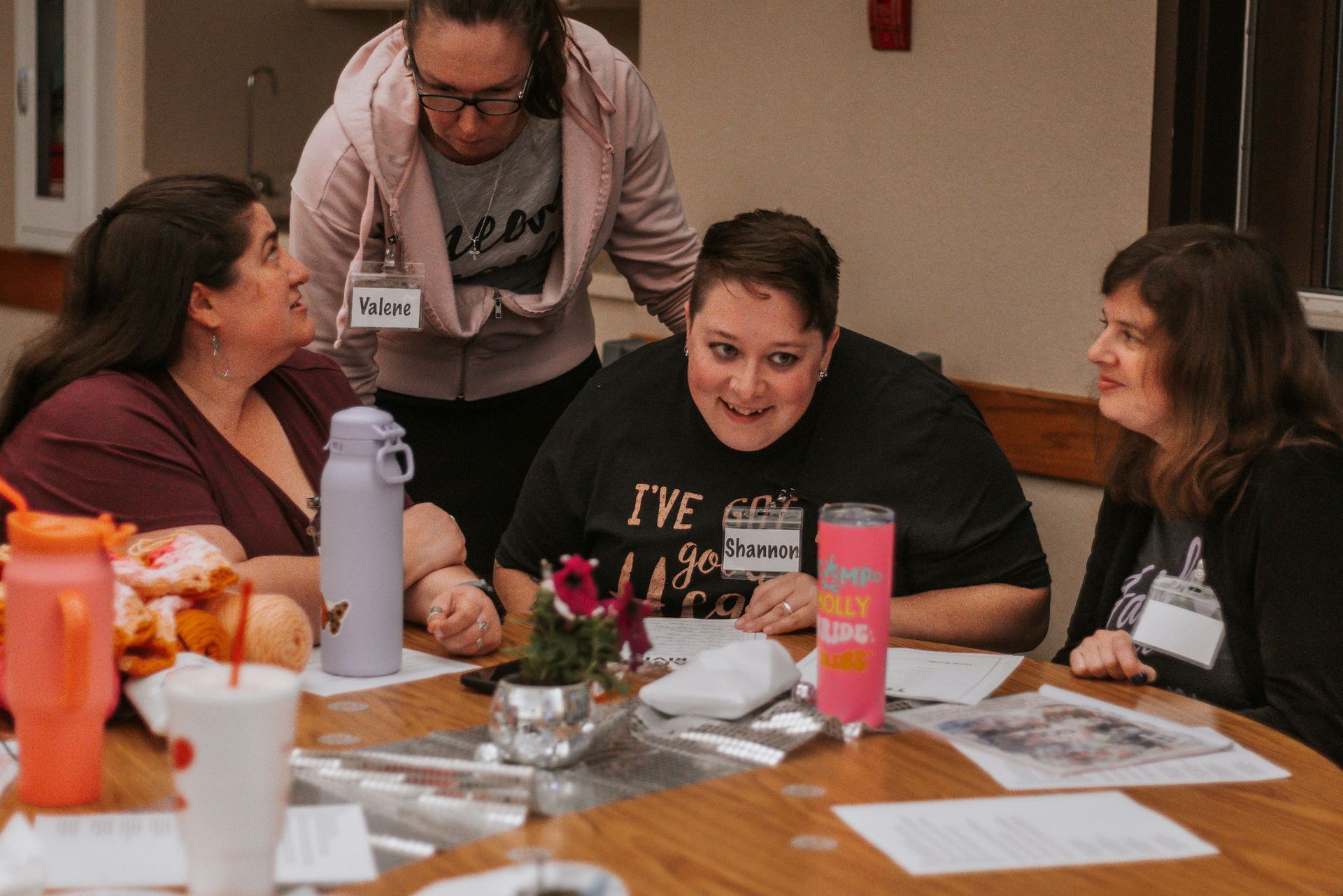 Four women at a table with papers, one looking surprised. 