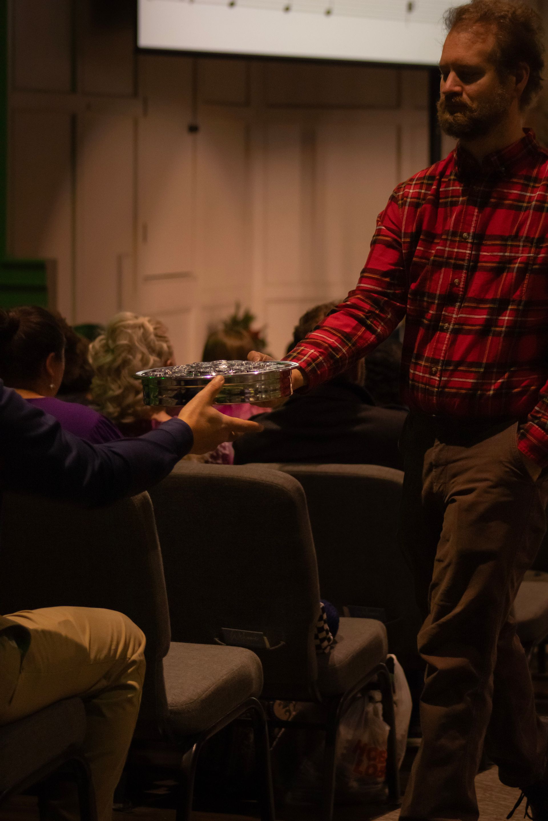 A man in a red plaid shirt is standing in front of a group of people sitting in chairs.