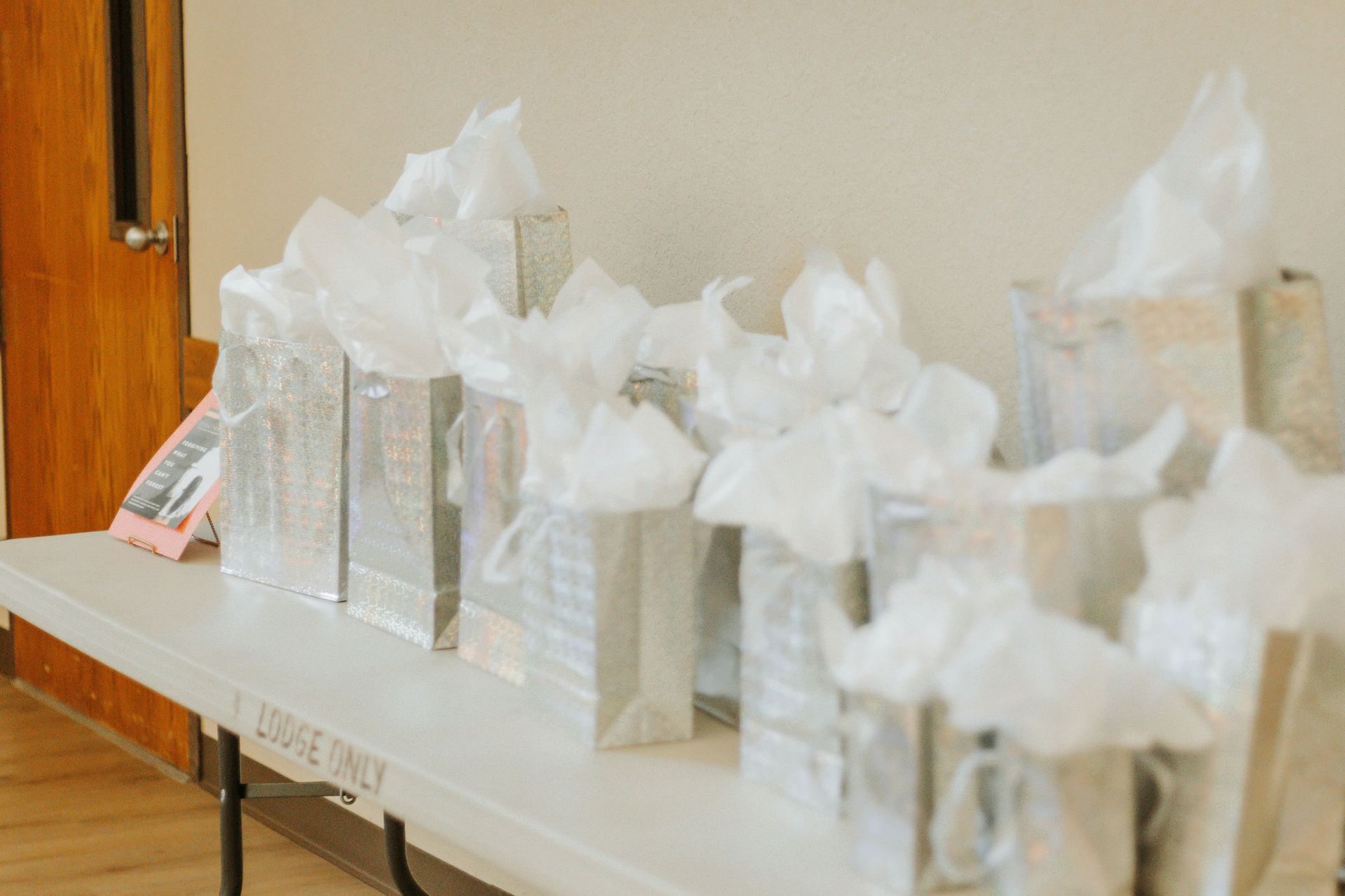 Gift bags on a white table, filled with tissue paper, against a beige wall.