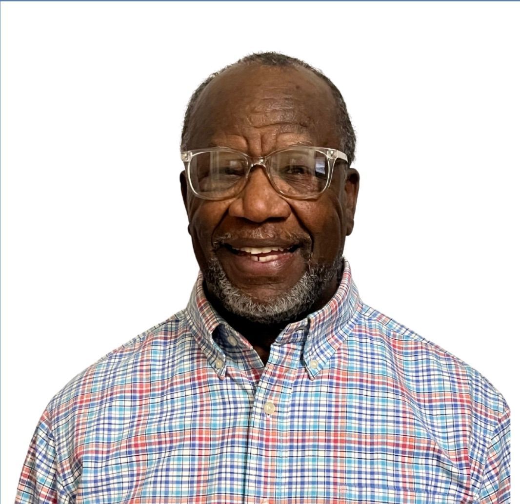 A man wearing a blue sweater and white shirt smiles for the camera