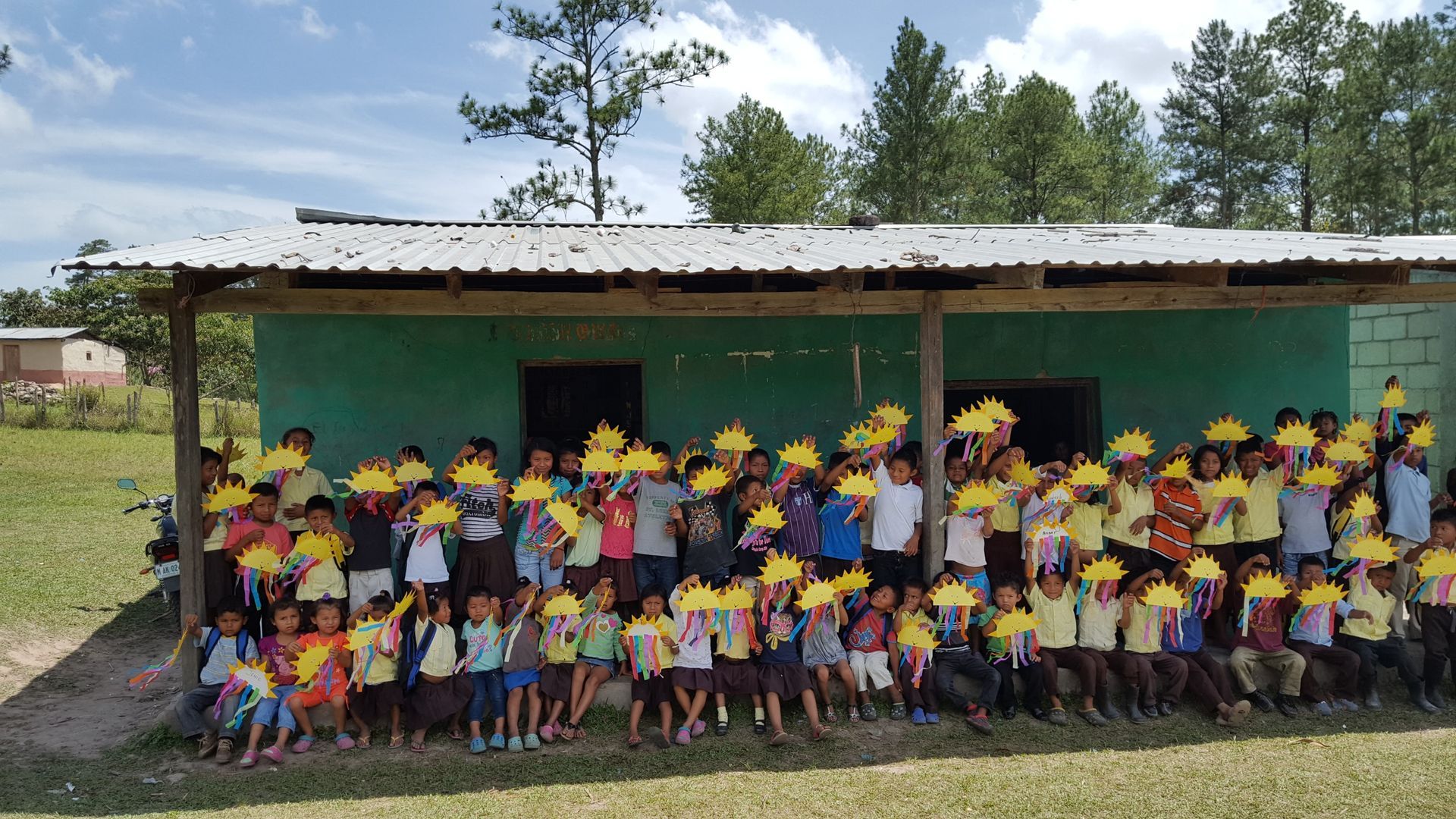 A large group of children are posing for a picture in front of a green building.