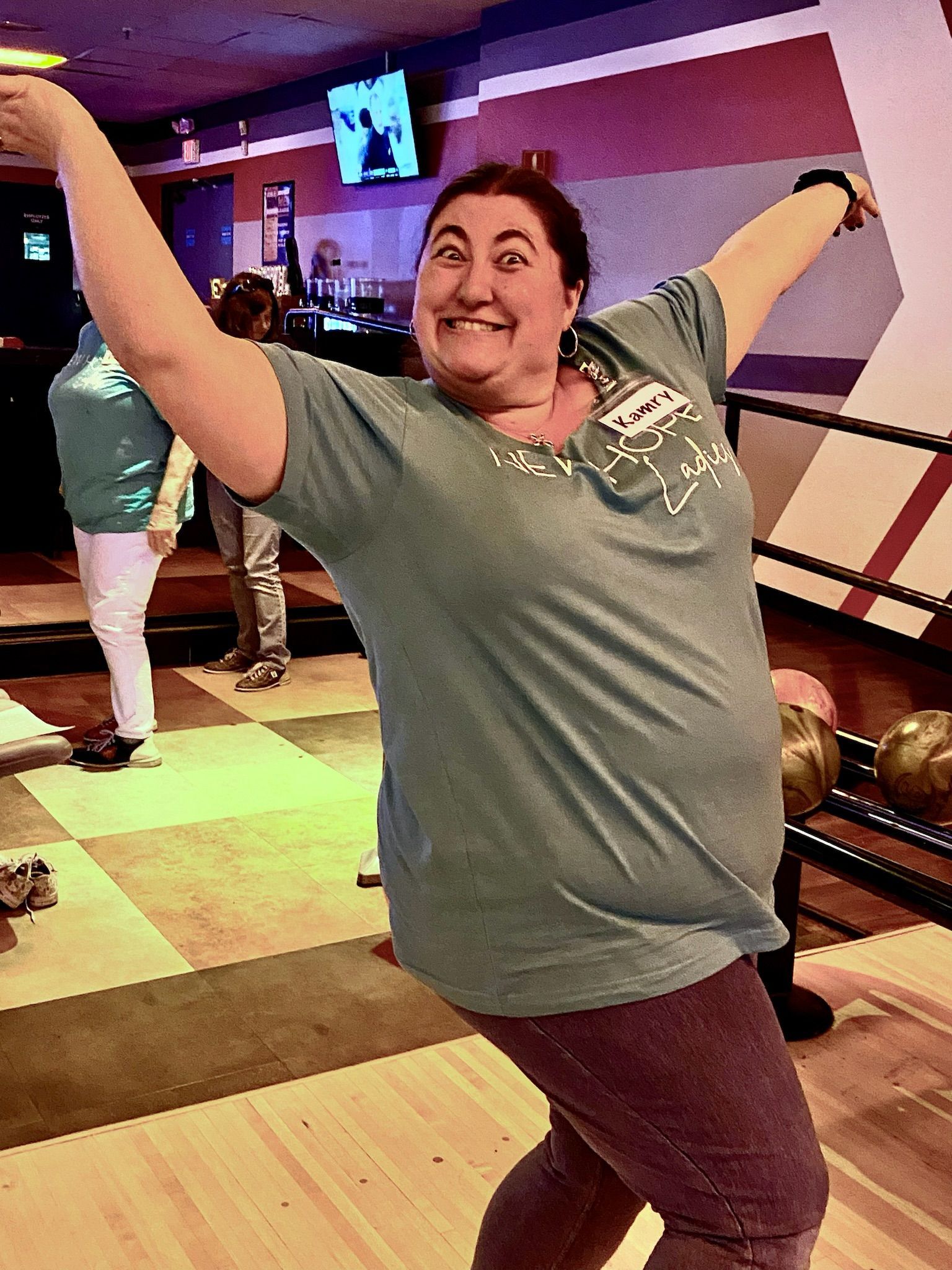 A woman is standing on a bowling alley with her arms outstretched.