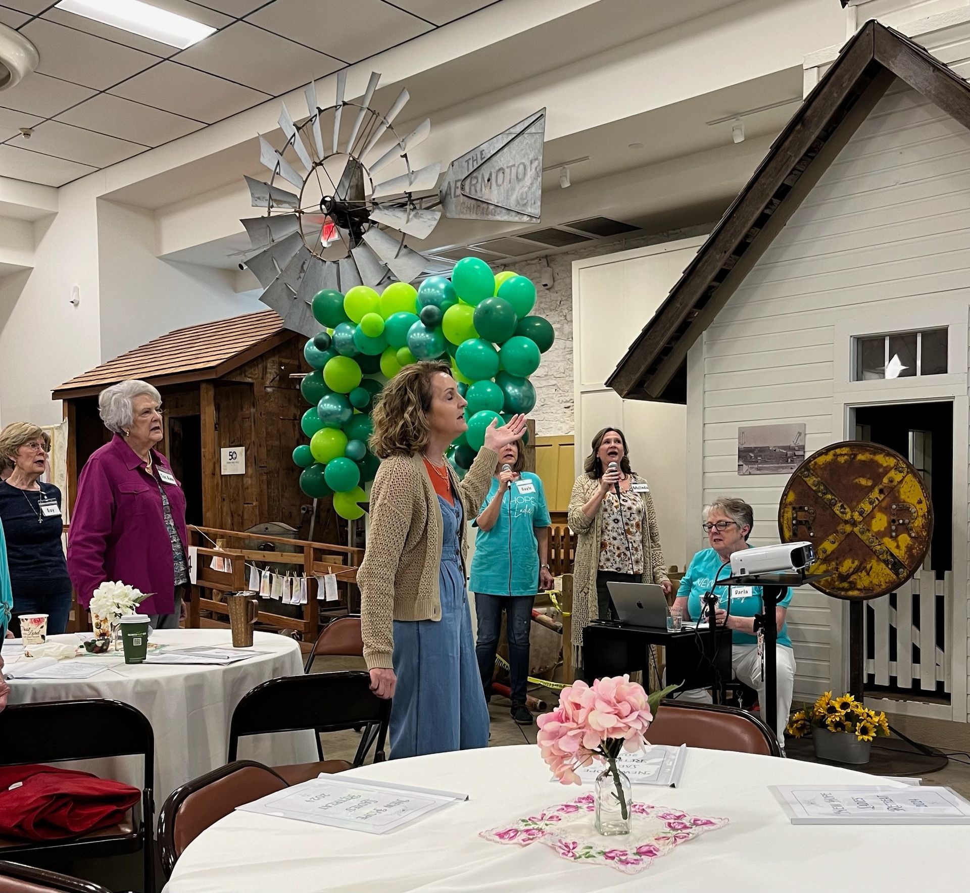 A group of people standing around tables with balloons and a windmill in the background