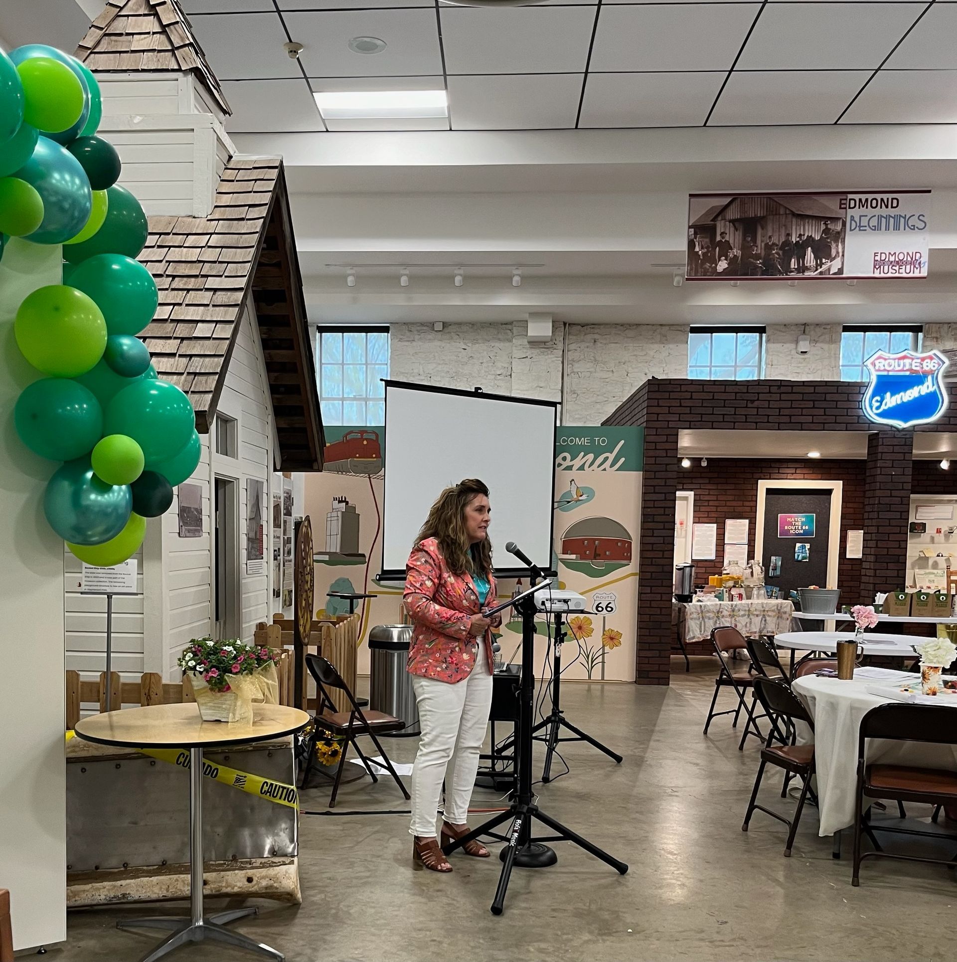 A woman is standing in front of a projector screen in a large room.