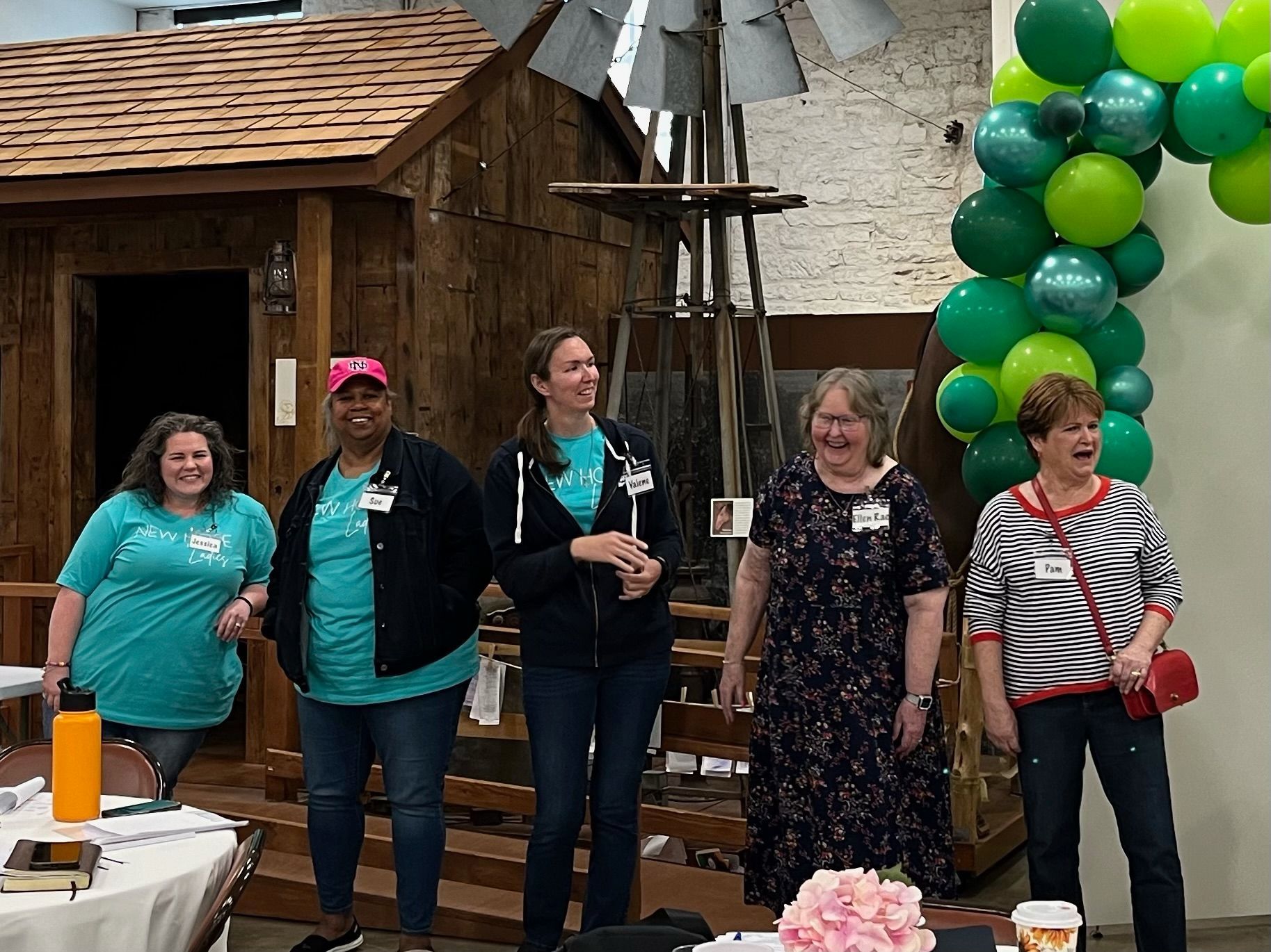 A group of women are standing next to each other in a room with balloons.