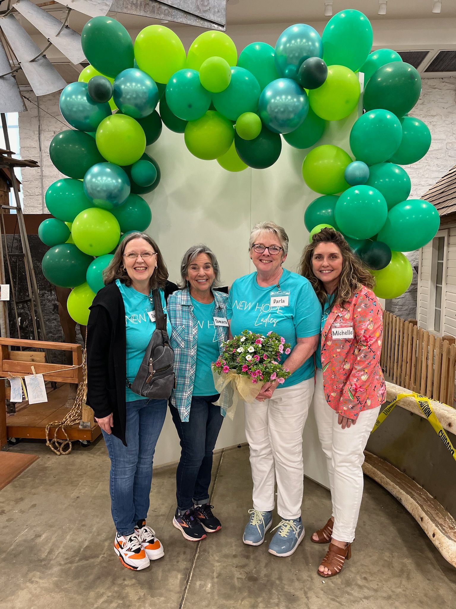 A group of women are posing for a picture in front of a green balloon arch.