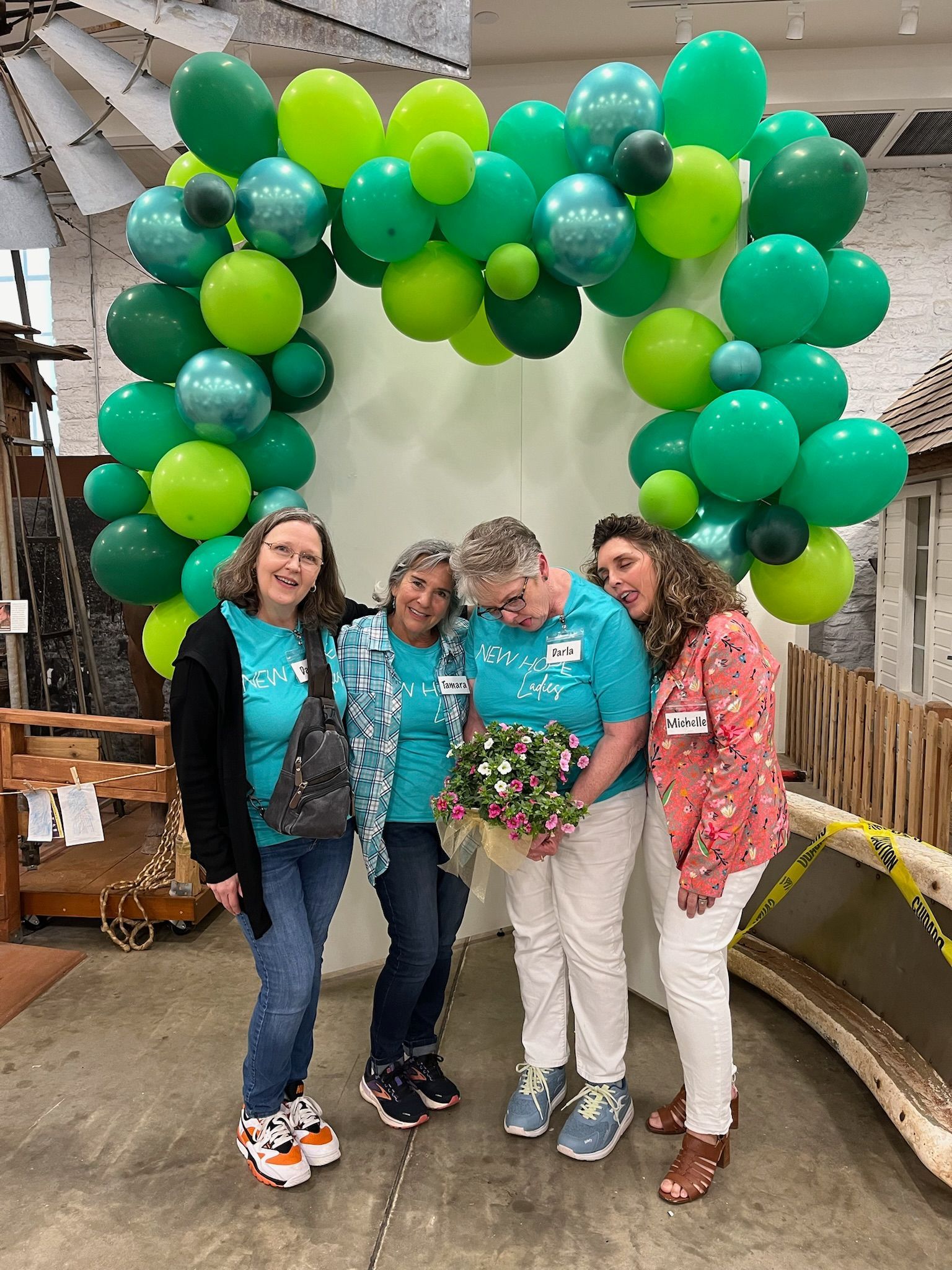 A group of women are posing for a picture in front of a green balloon arch.