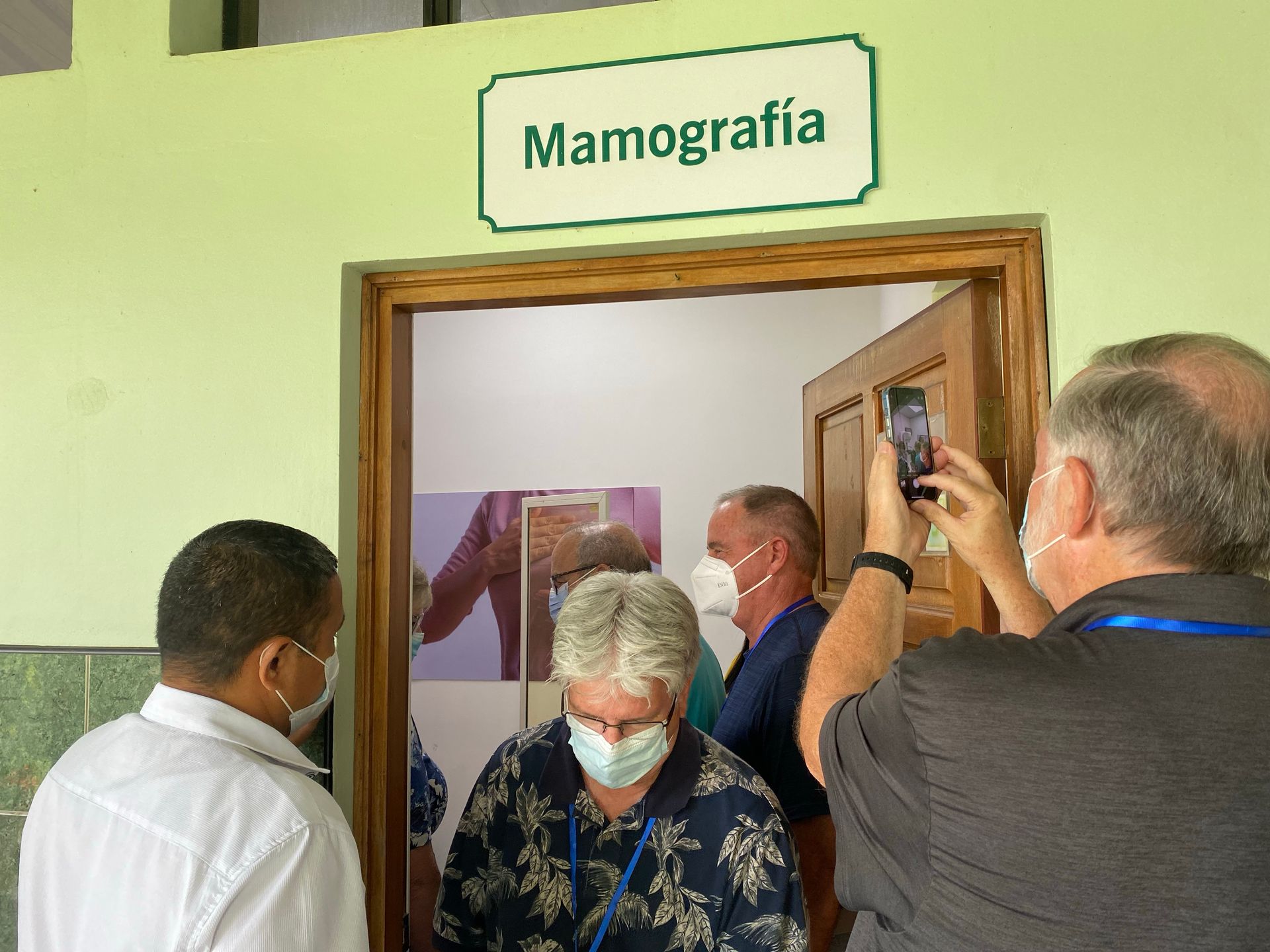 A man is taking a picture of a group of people in a room with a sign that says mamografia