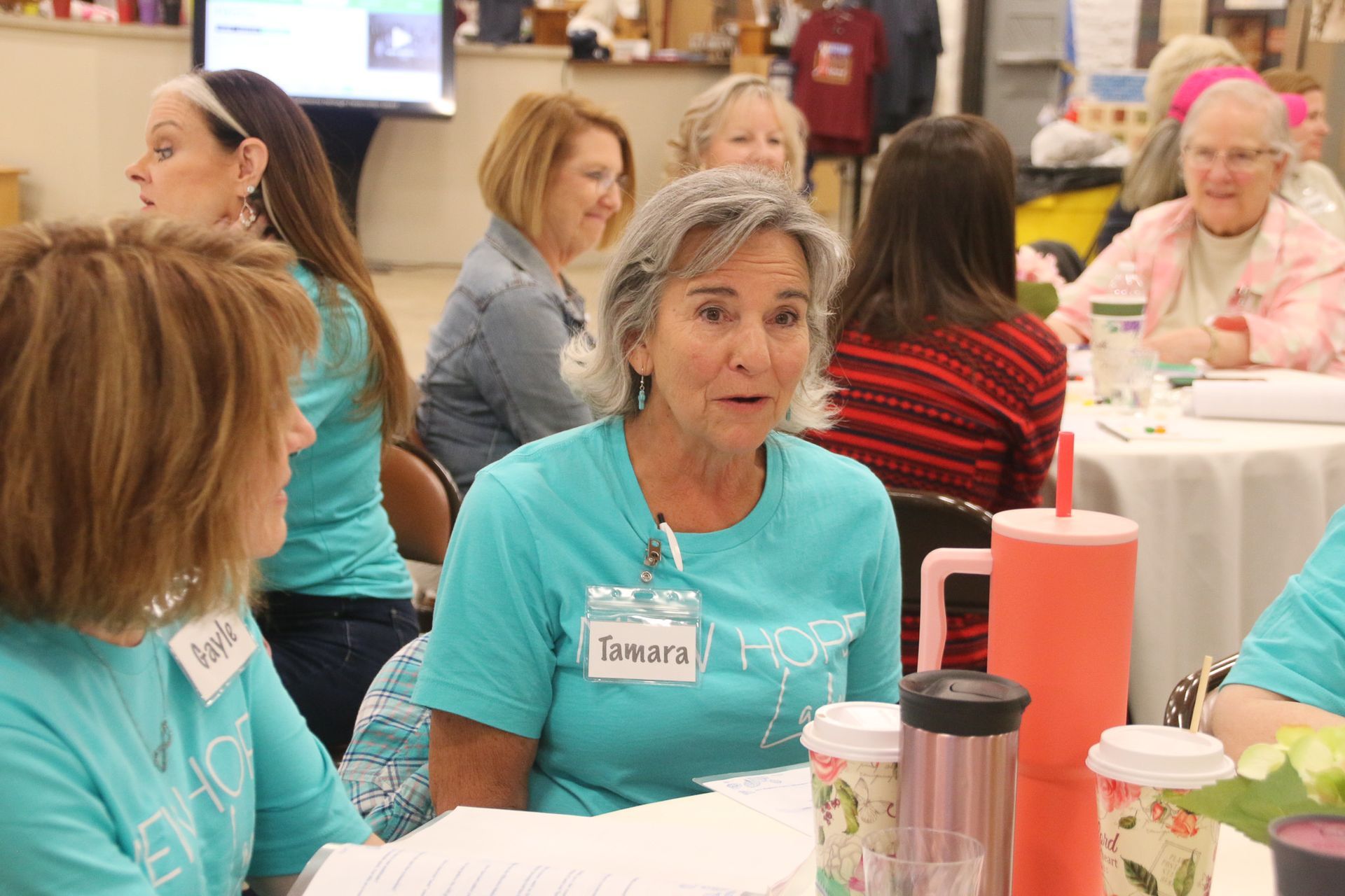 A group of women are sitting at tables talking to each other.