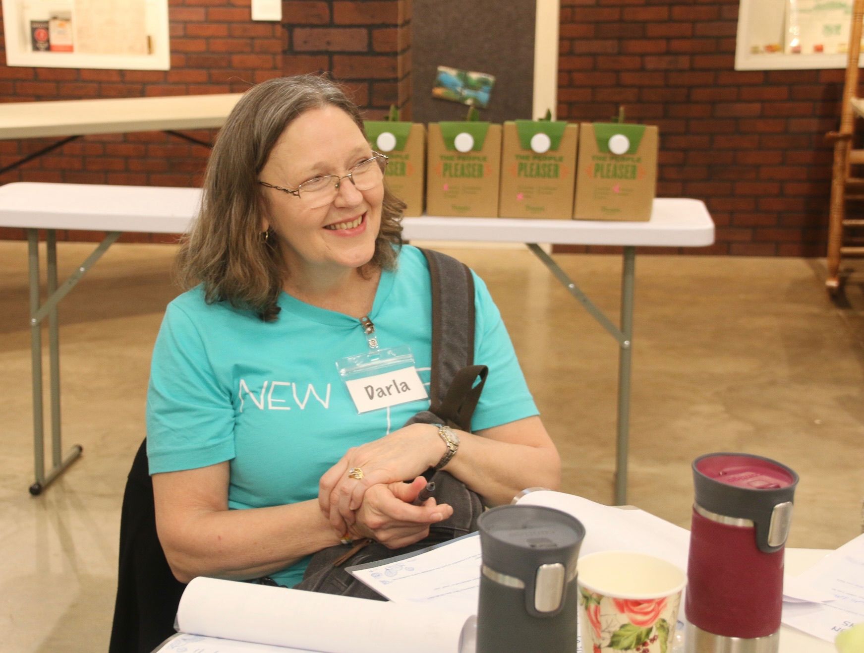 A woman wearing a blue shirt that says new is sitting at a table