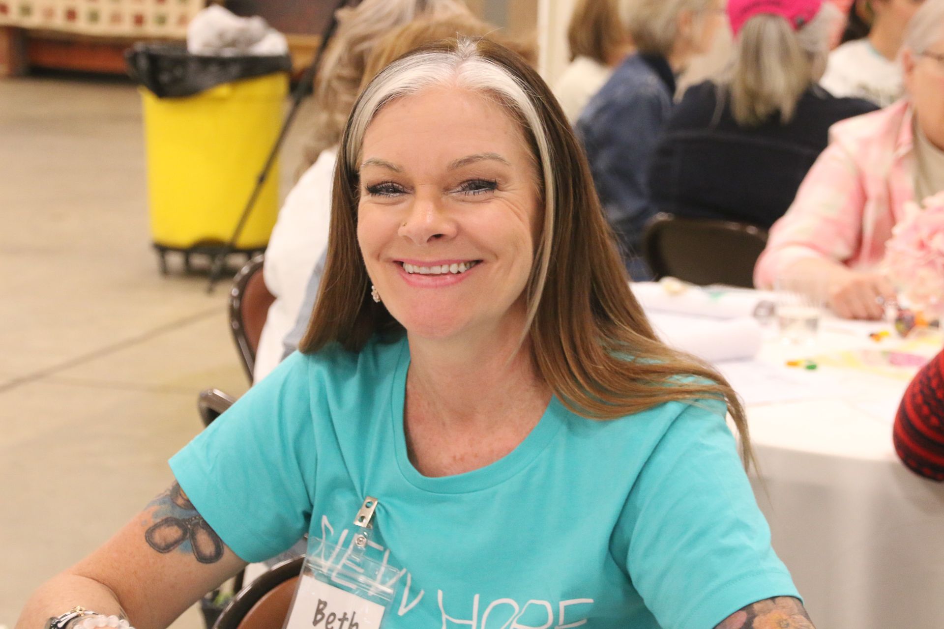 A woman in a blue shirt is smiling while sitting at a table.