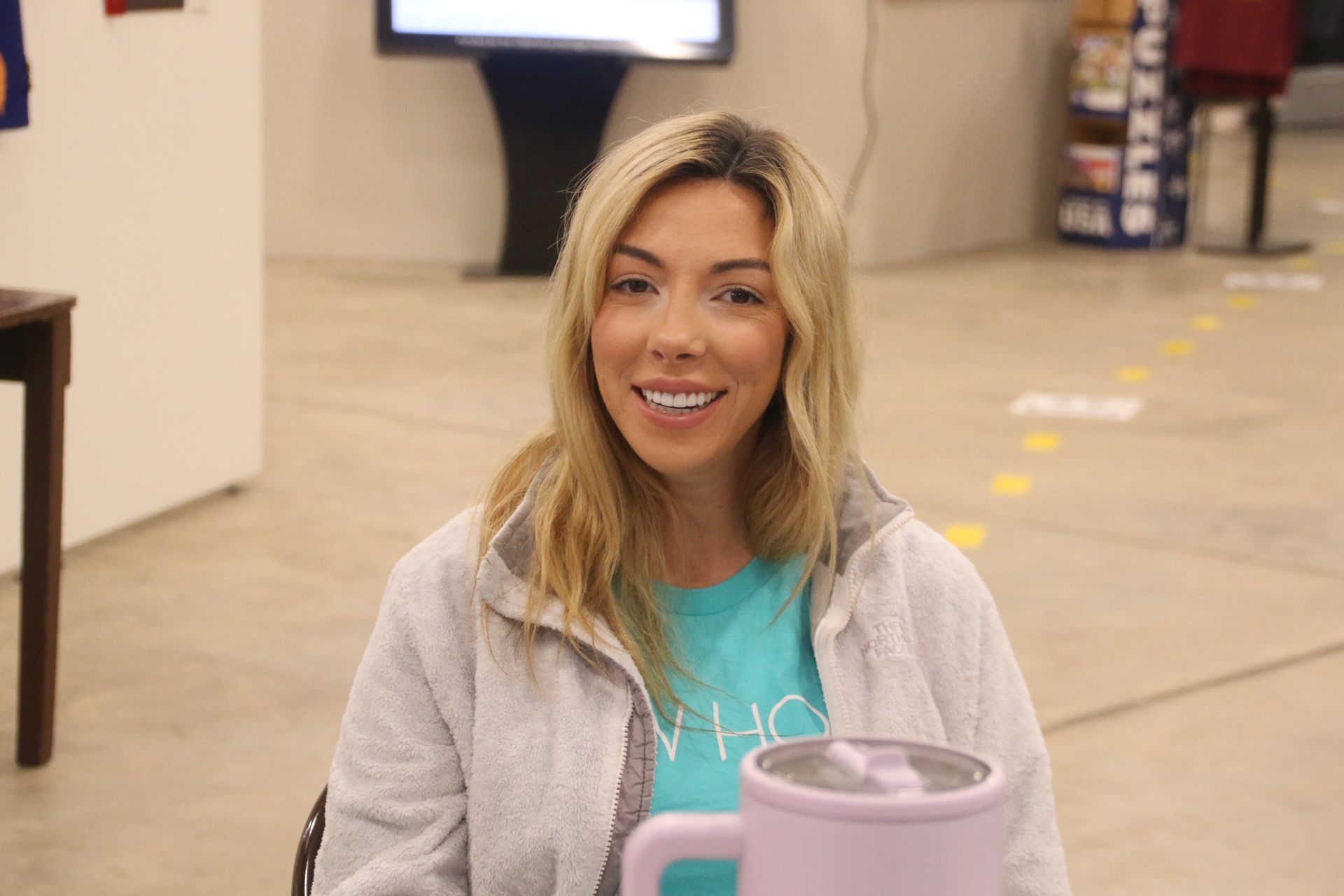 A woman is sitting in a chair holding a mug and smiling.