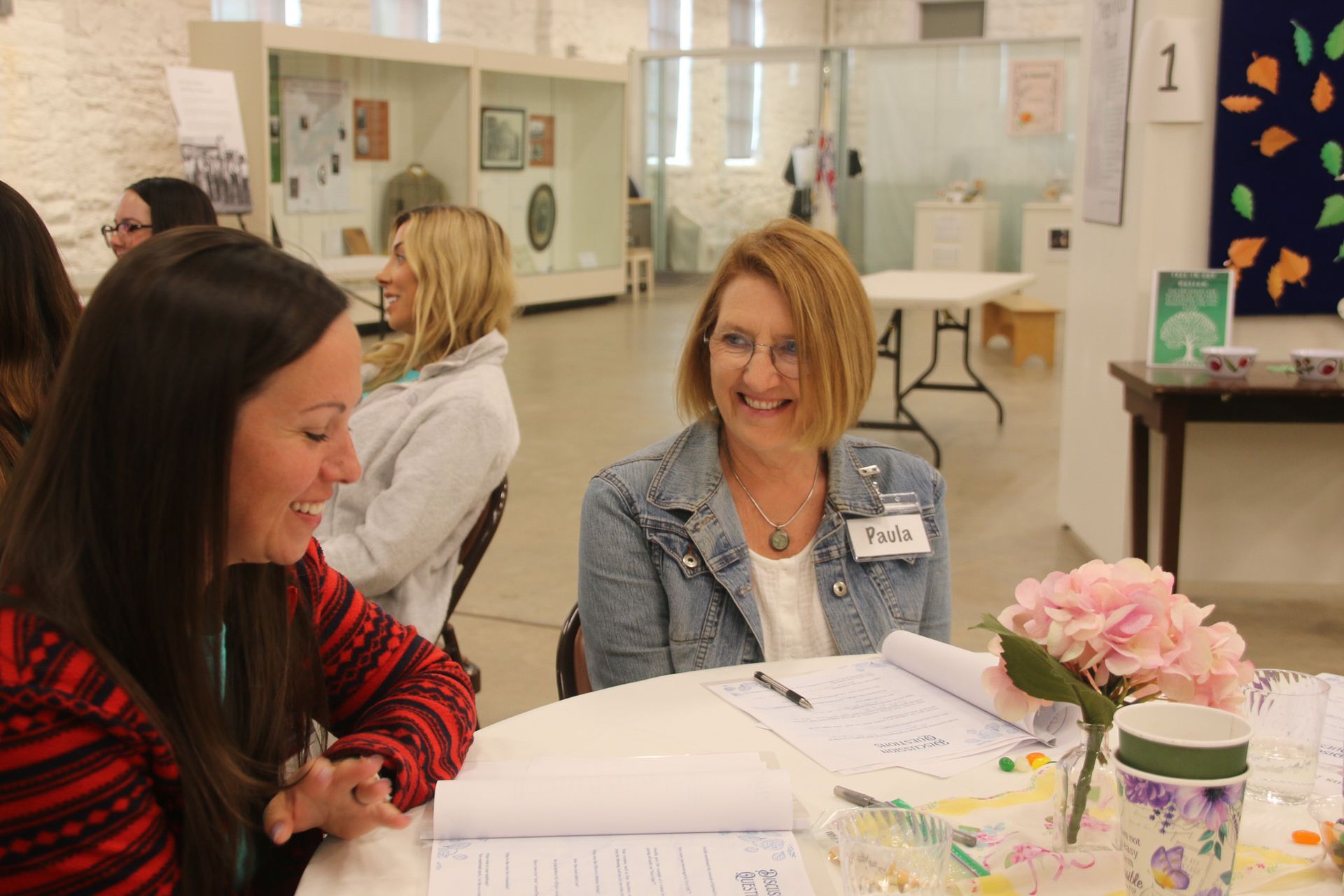 Two women are sitting at a table talking to each other.