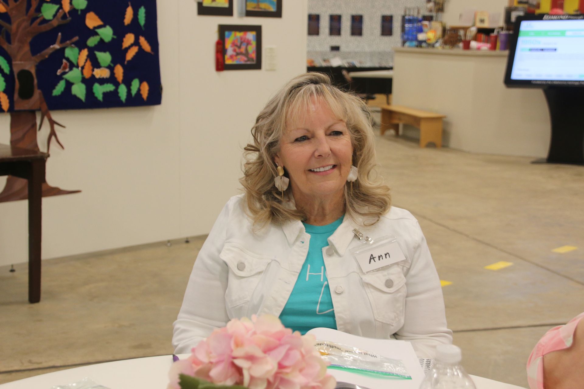 A woman is sitting at a table with flowers and smiling.