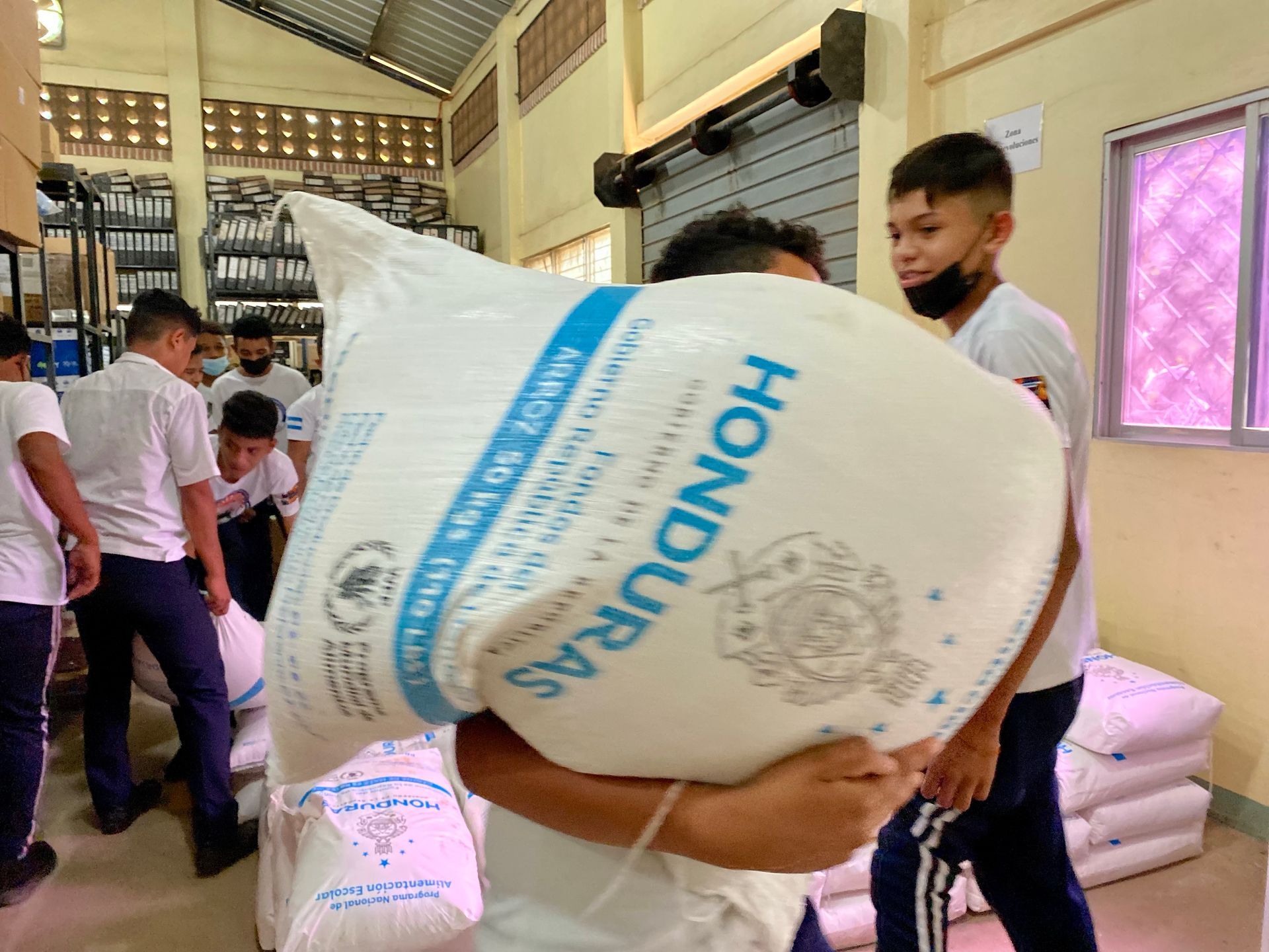 A man is carrying a large bag of honduras rice.