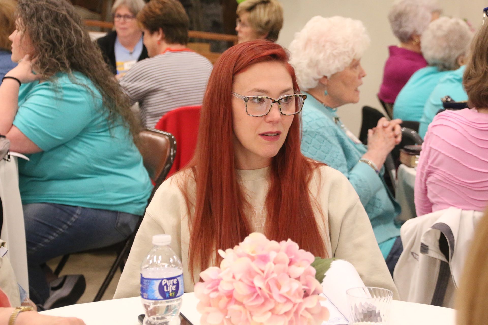 A woman with red hair is sitting at a table with a bottle of water.