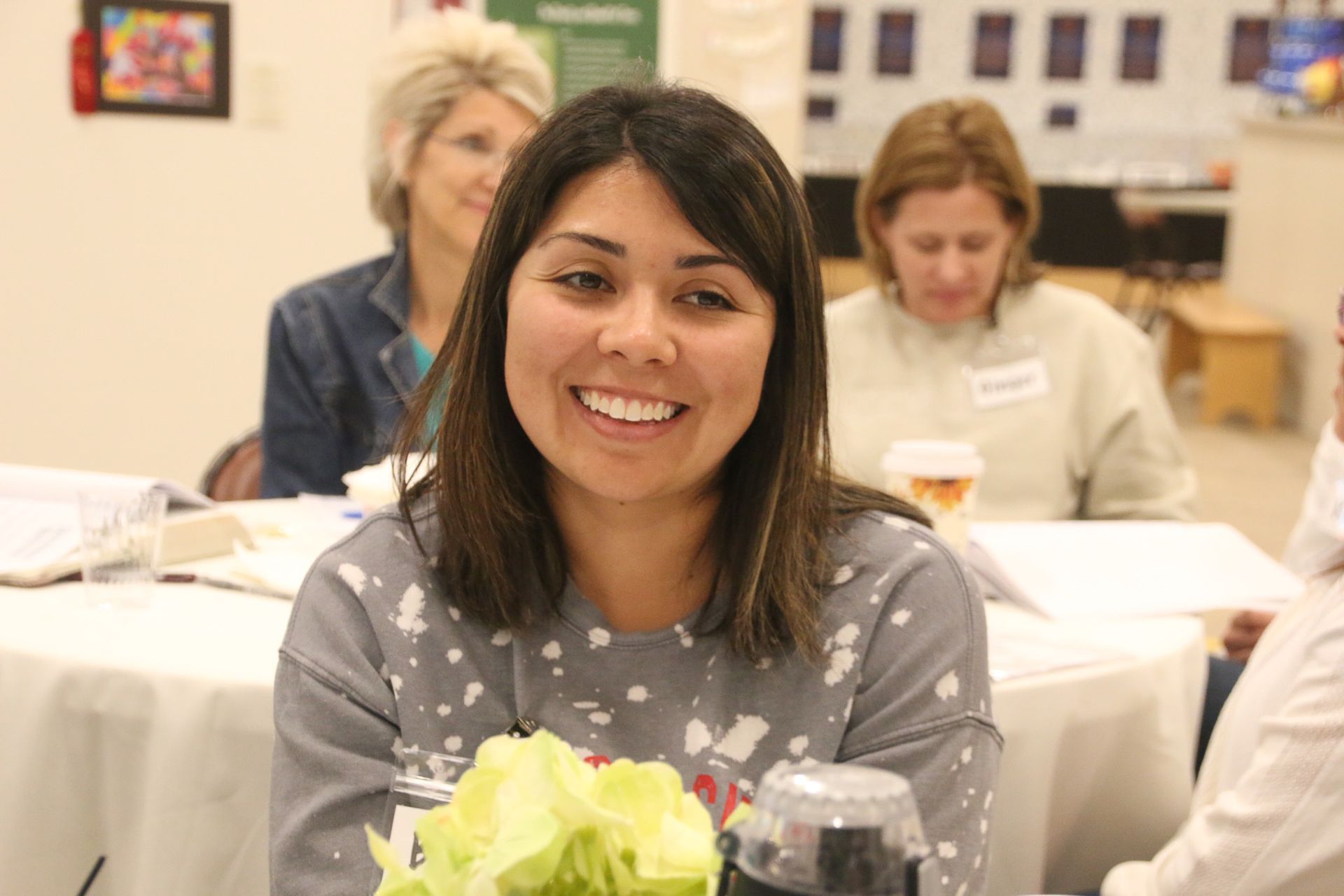 A woman is smiling while sitting at a table with other people.