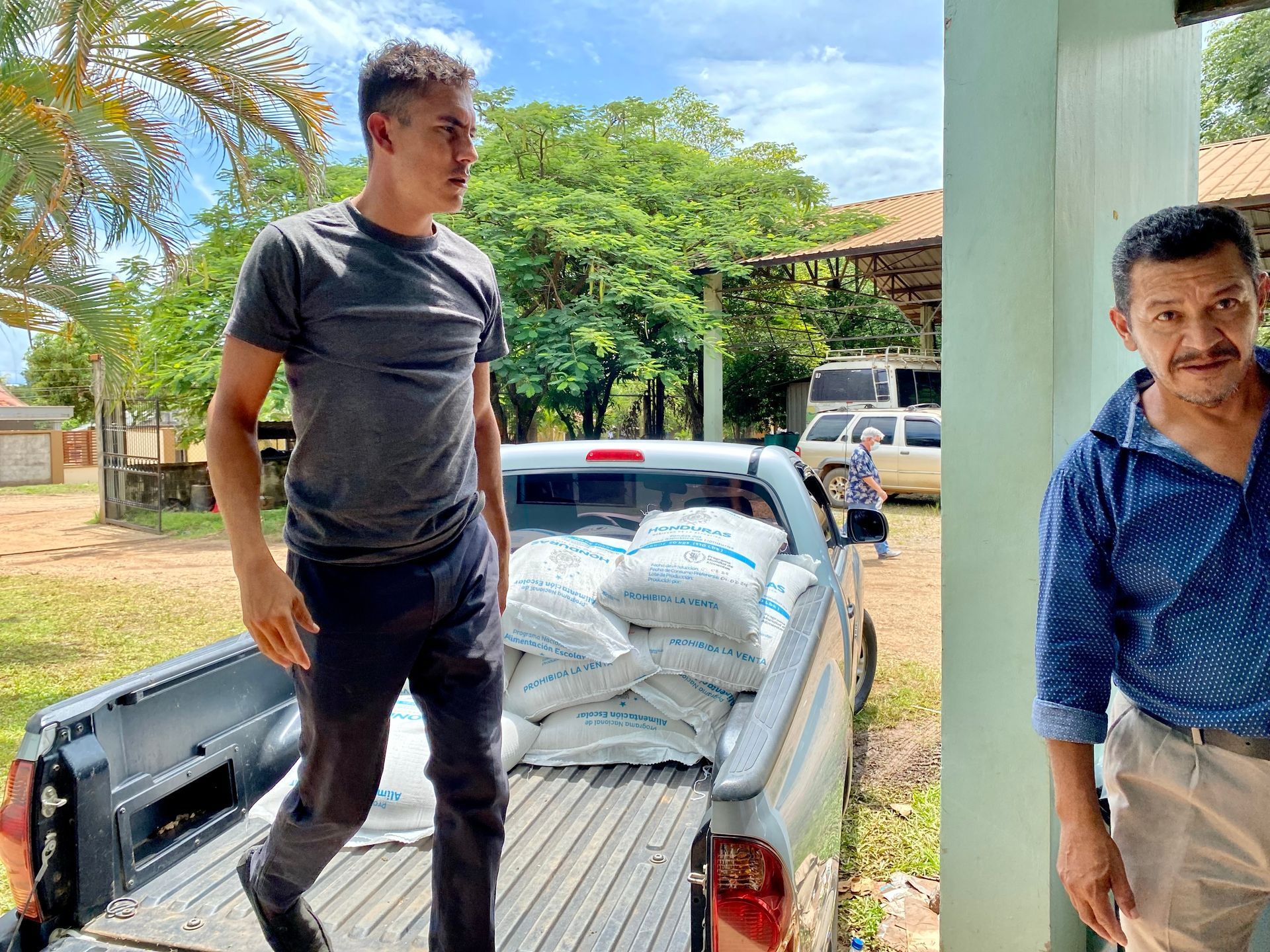 Two men are standing next to a truck with bags of food in the back.