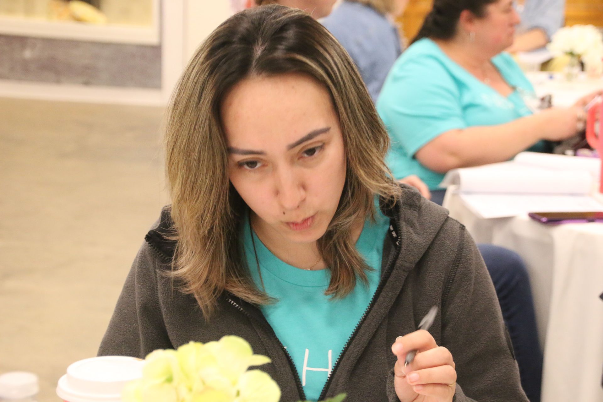 A woman in a blue shirt is sitting at a table with a pen in her hand.