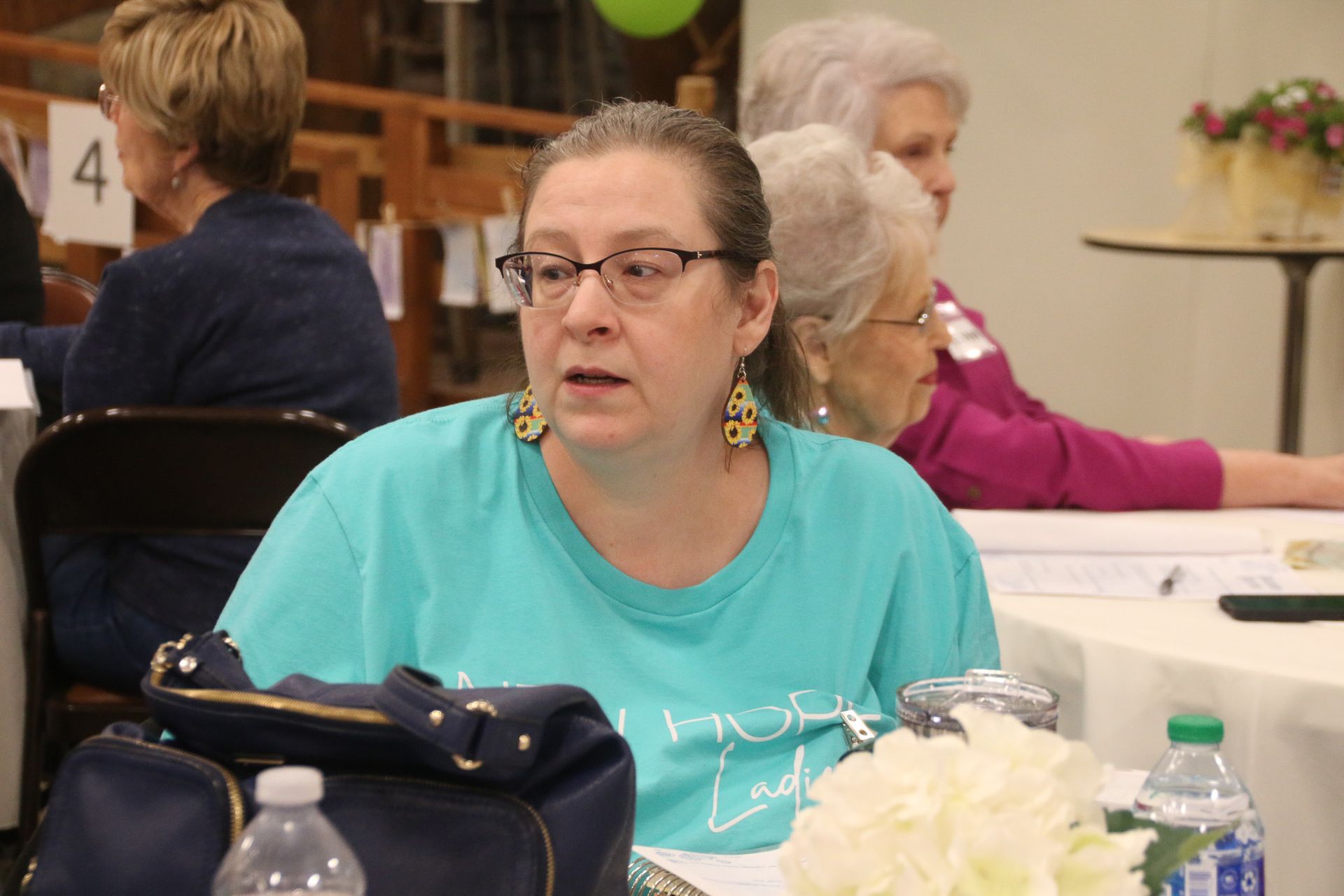 A woman wearing glasses and a blue shirt is sitting at a table.