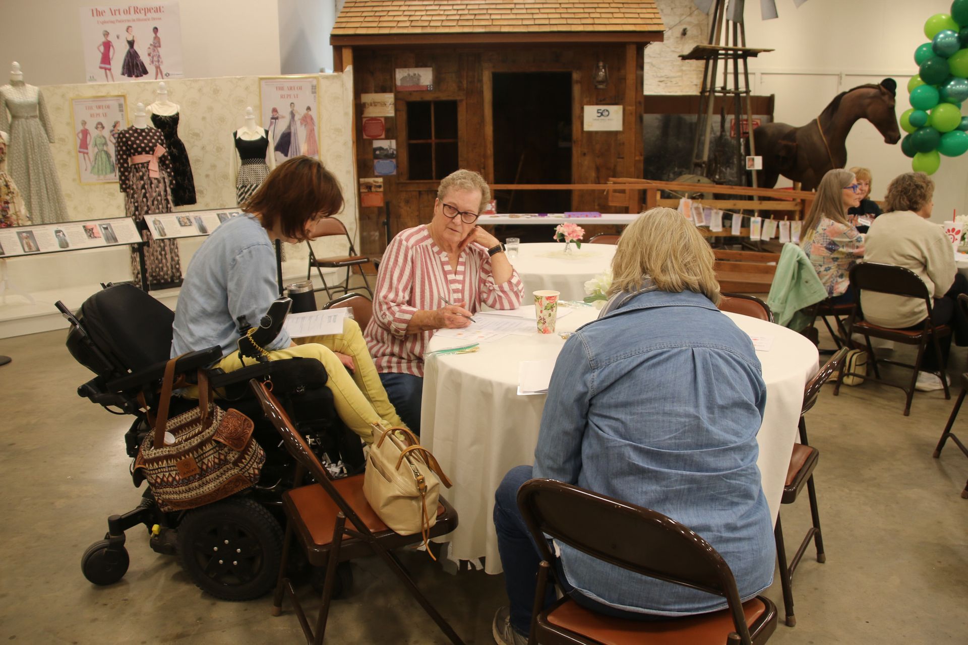 A group of people are sitting at tables in a room with a horse in the background.