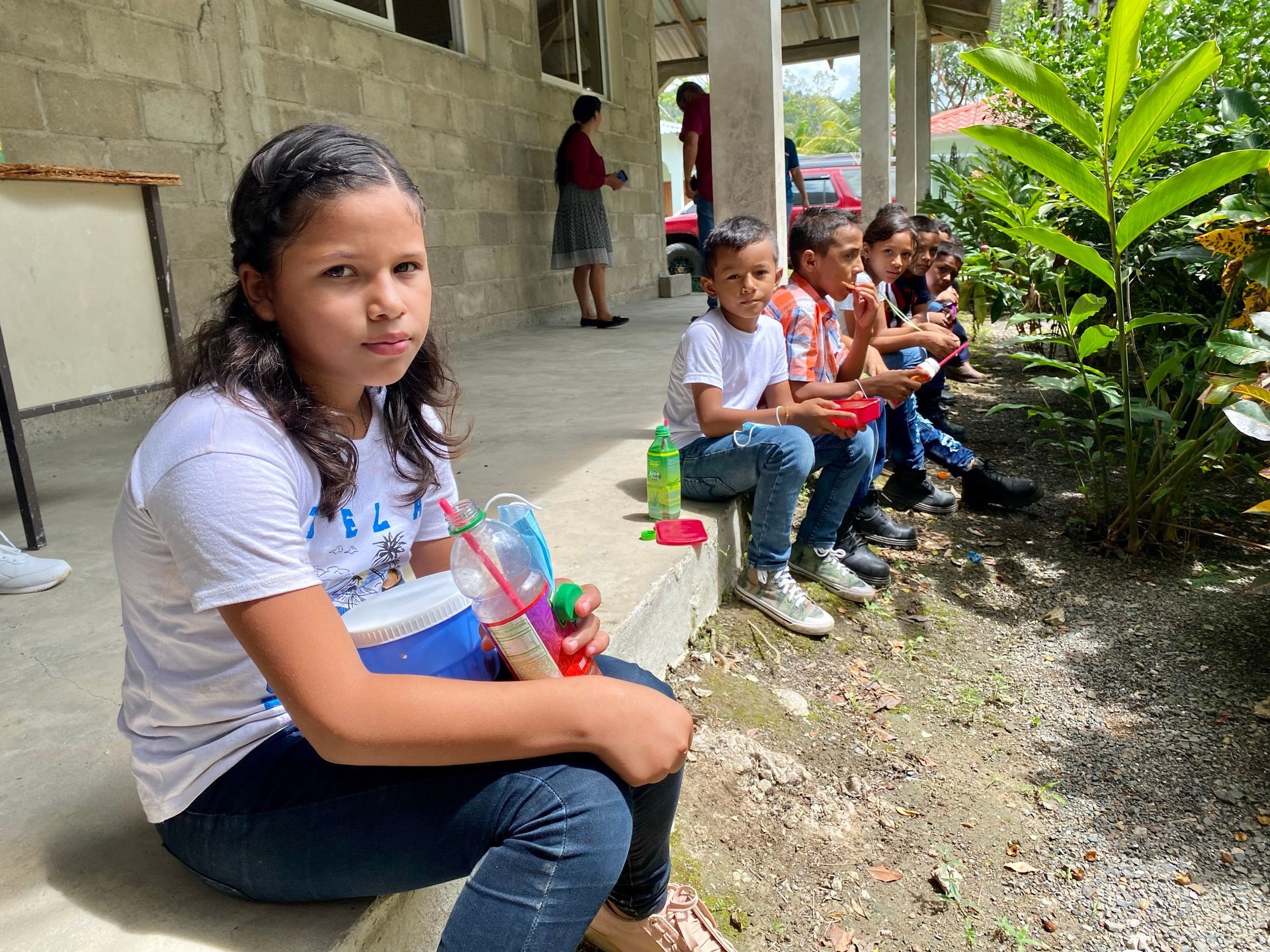 A group of children are sitting on the ground eating food.