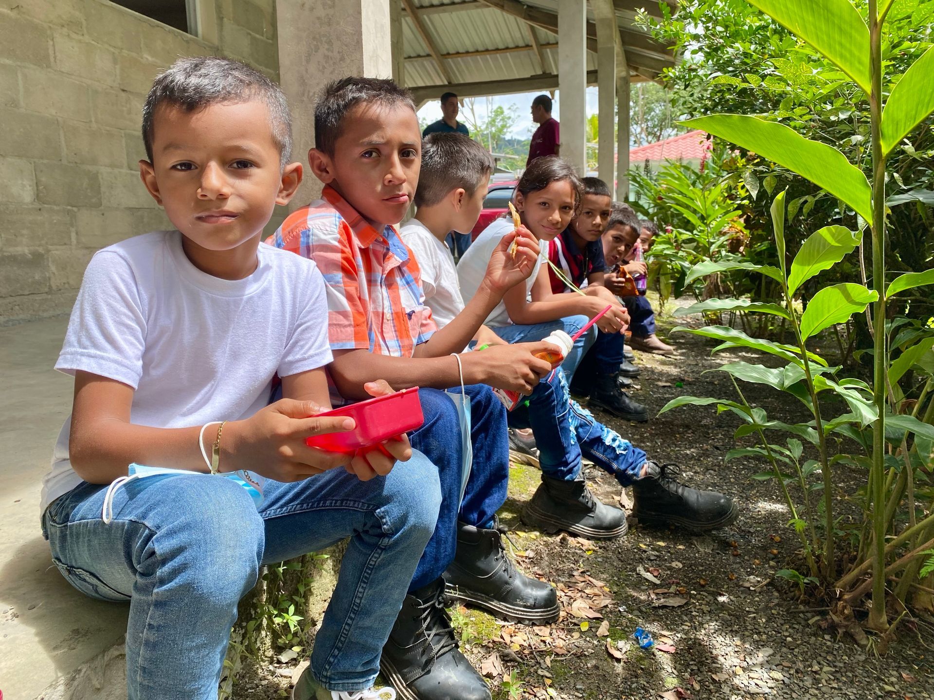 A group of children are sitting on the ground eating ice cream.