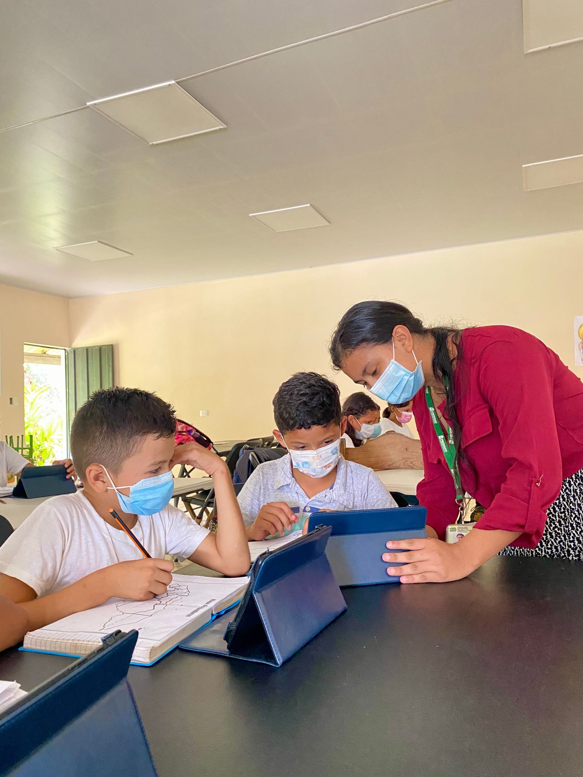 A teacher is helping two students with their homework in a classroom.