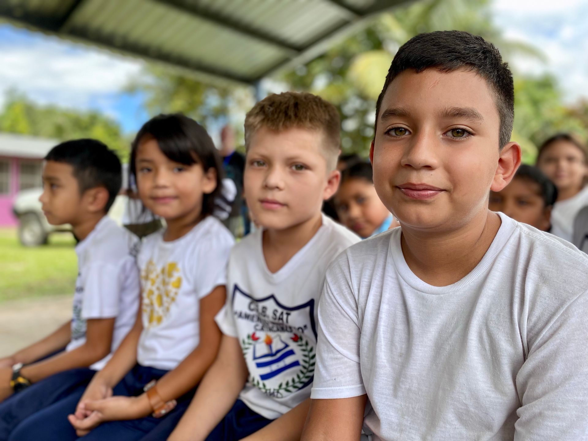 A group of children are sitting next to each other under a canopy.
