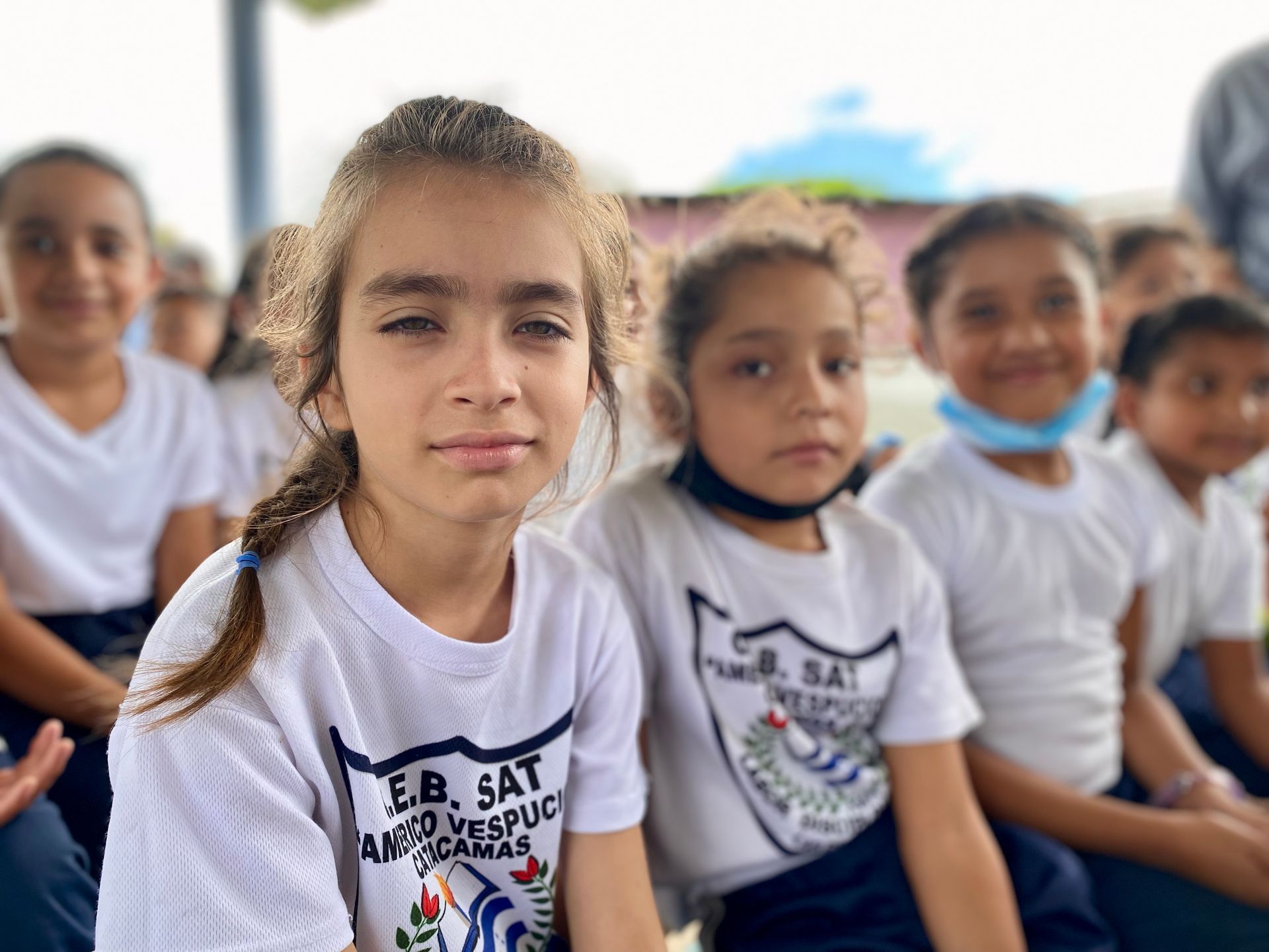 A group of young girls are sitting in a row wearing e.b. sat shirts.