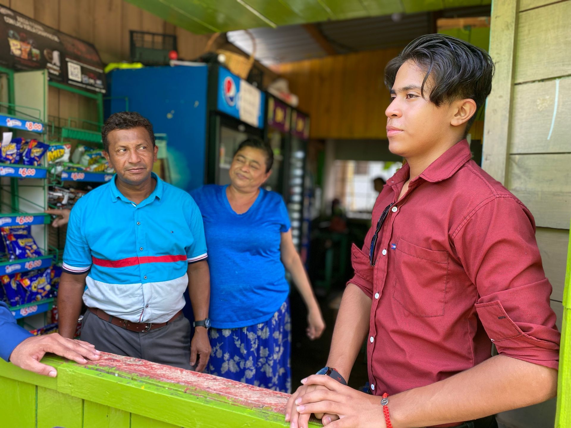 A man in a red shirt is standing next to a woman and a man in a blue shirt.