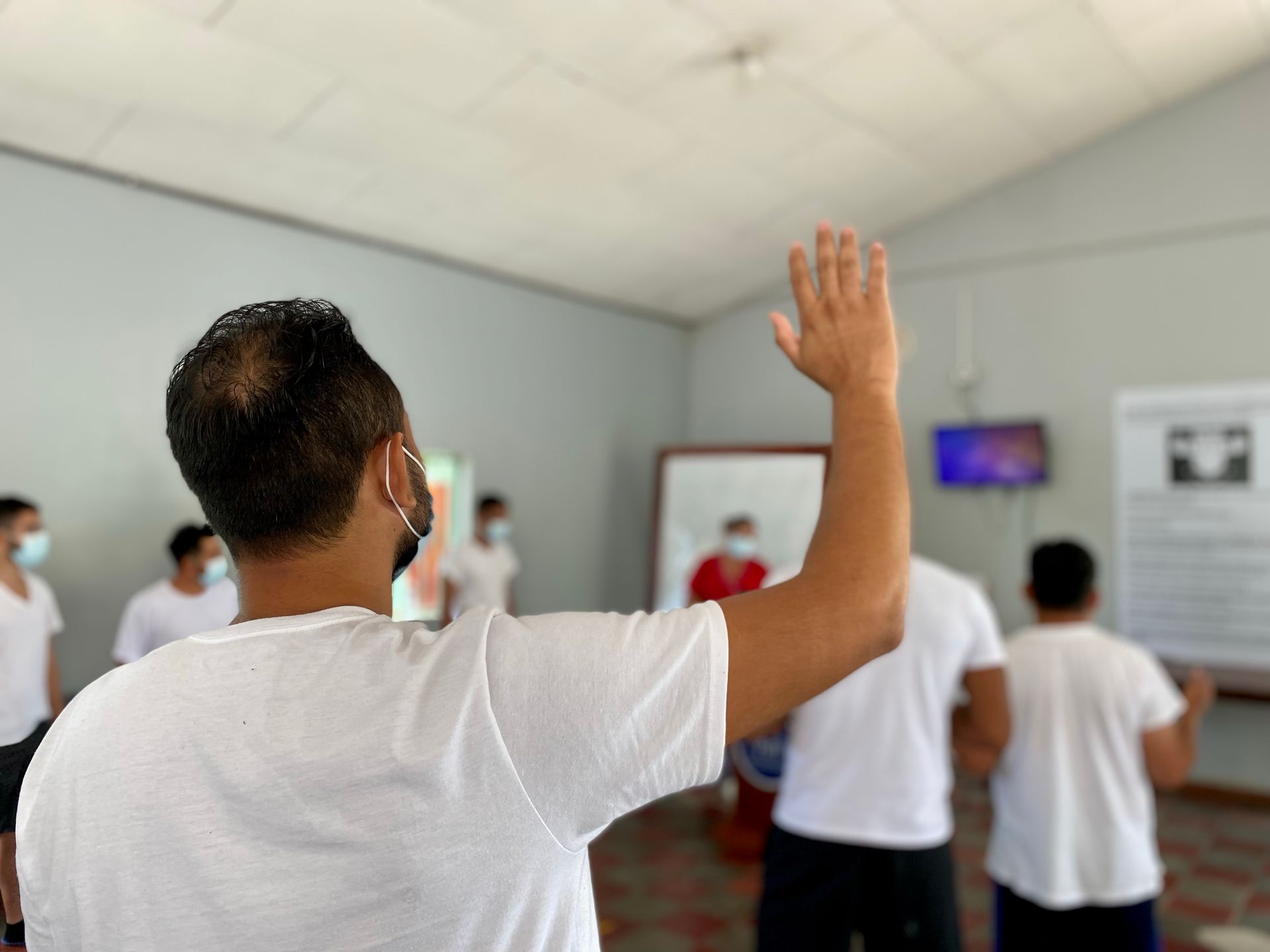 A man in a white shirt is raising his hand in a room.