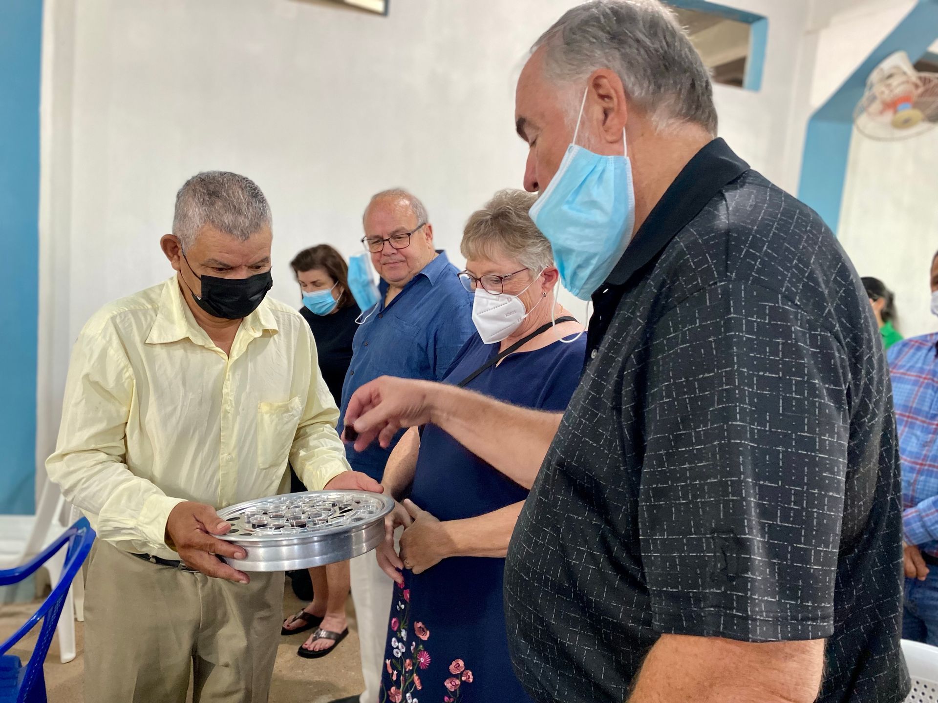 A group of people wearing face masks are standing around a table.