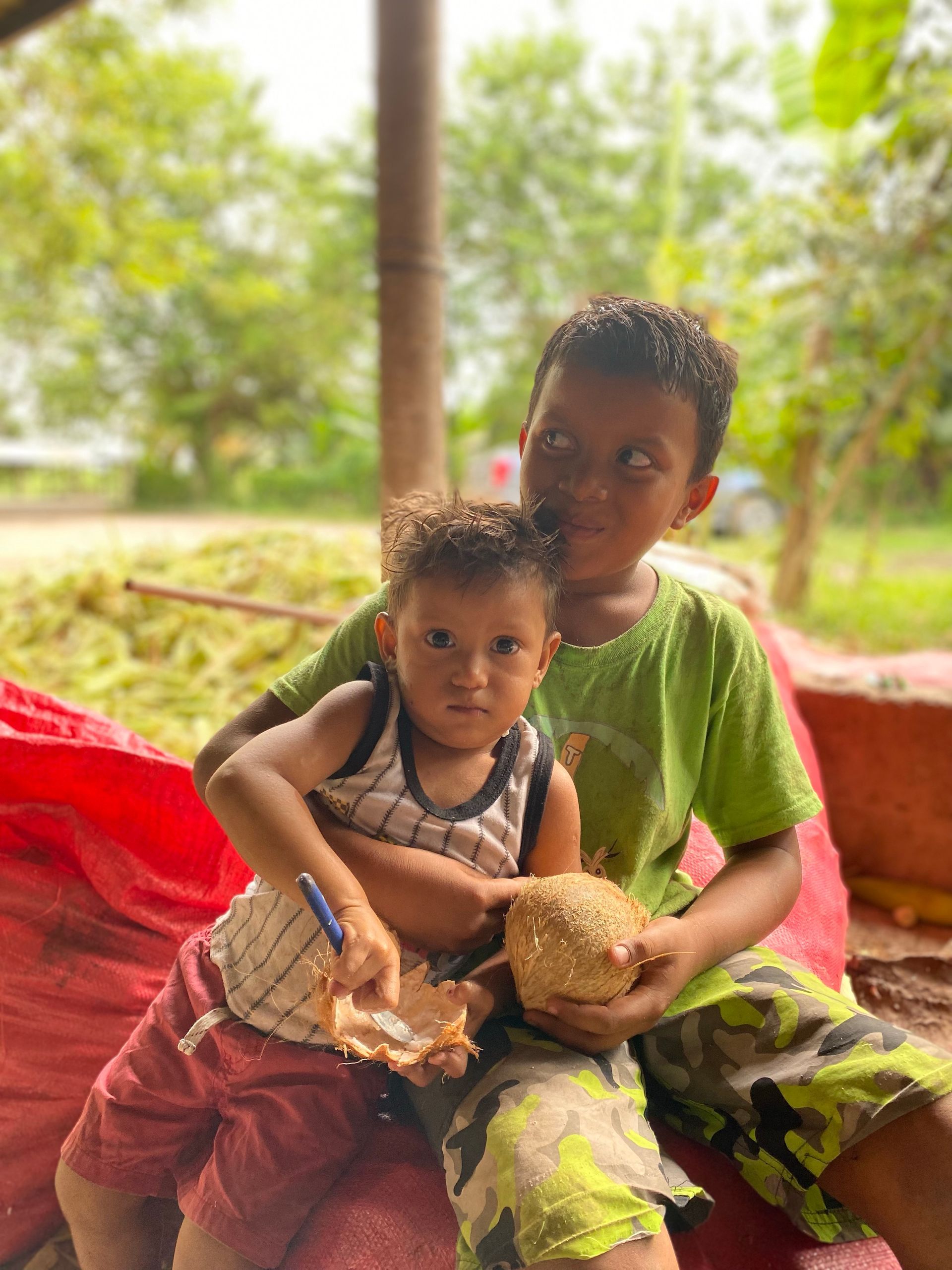 Two young boys are sitting next to each other holding a coconut.