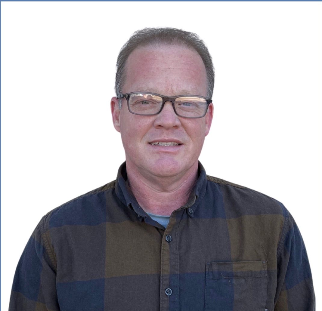 Man with glasses wearing a plaid shirt, smiling, head and shoulders shot against a white background.