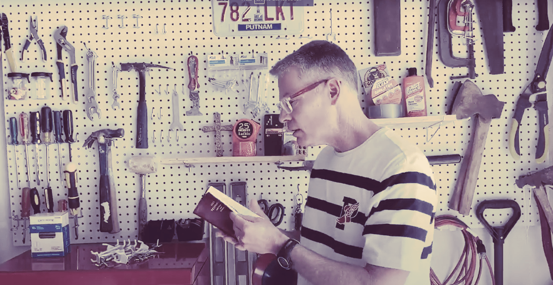 A man in a striped shirt is reading a book in a garage.