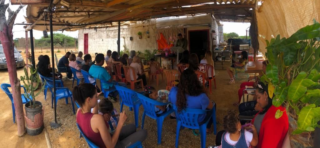 A group of people are sitting in blue chairs under a canopy.