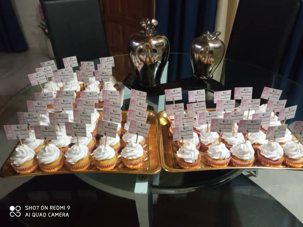 Two trays of cupcakes with white frosting on a table.