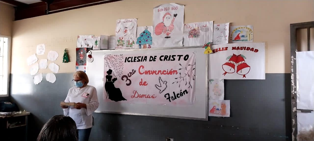 A woman wearing a mask is standing in front of a white board in a classroom.