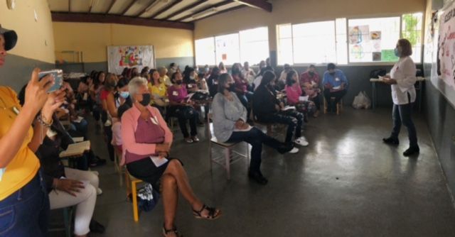A woman is standing in front of a large group of people sitting in chairs.
