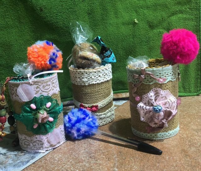 Three cans with flowers on them are sitting on a table next to a pen.