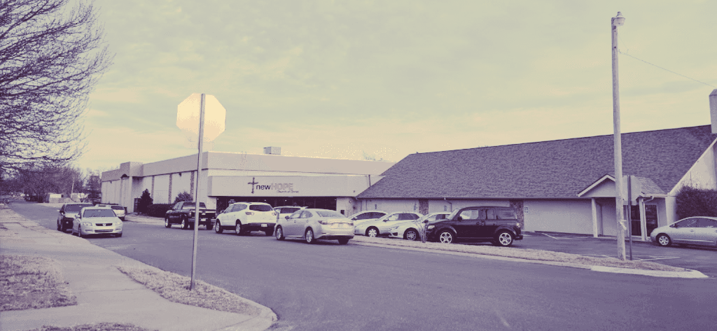 A row of cars are parked on the side of the road in front of a building.
