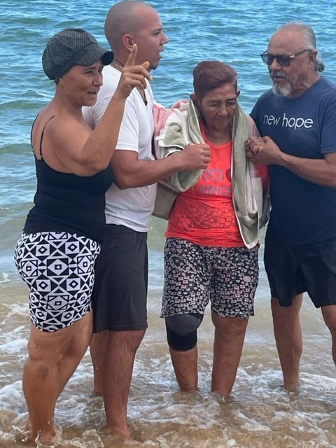 A group of people are standing in the water on a beach.