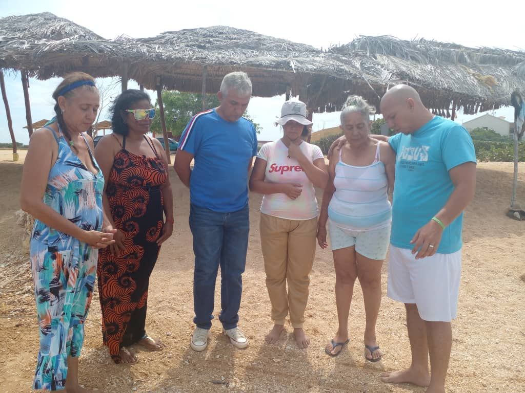 A group of people are standing in front of a thatched roof.