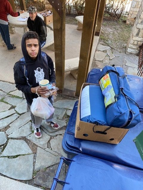 A boy standing next to a trash can holding a bag of food