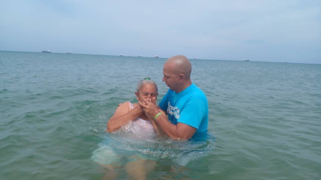 A man is baptizing a woman in the ocean.