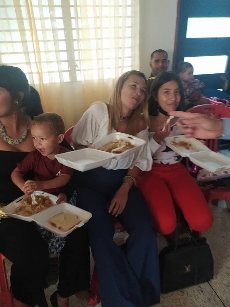 A group of people are sitting in a room eating food from styrofoam containers.