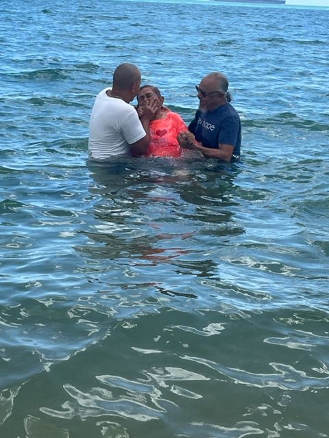 Two men are baptizing a woman in the ocean.