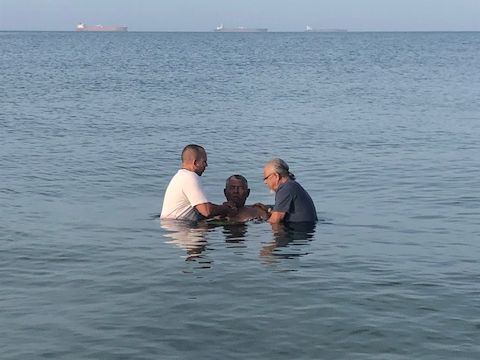A man is being baptised in the ocean by two other men.