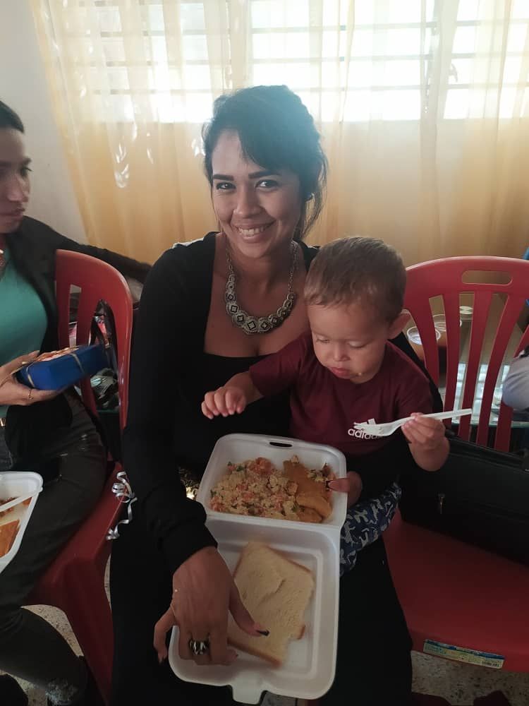 A woman is holding a baby and holding a styrofoam container of food.